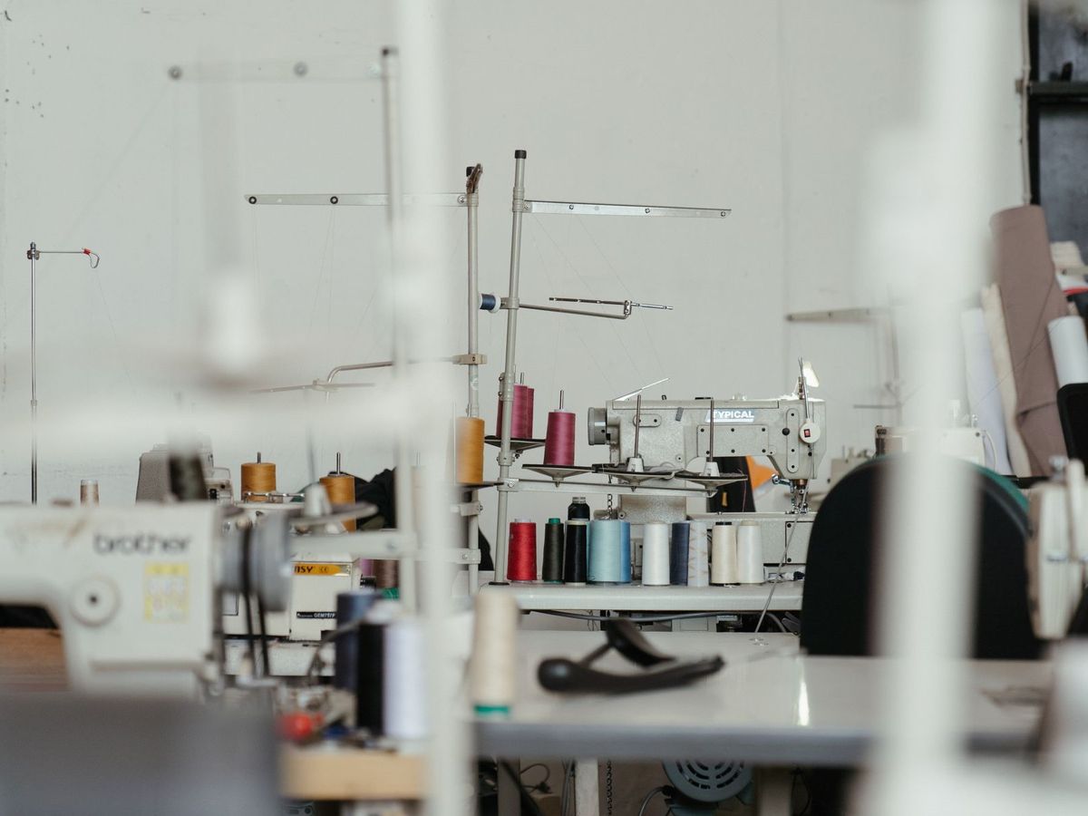 A garment workroom with rows of industrial sewing machines and spools of thread