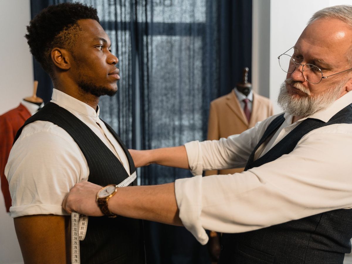 A tailor taking chest measurements over a waistcoat during a suit fitting