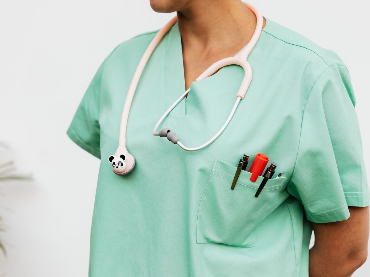 A healthcare worker in mint green scrubs with a stethoscope and pens in the chest pocket